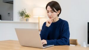 自宅のデスクでノートパソコンを使い、婚活掲示板の情報を真剣に読みつつ、思索にふける30代前半の日本人女性。落ち着いた照明と清潔感のある部屋の雰囲気。