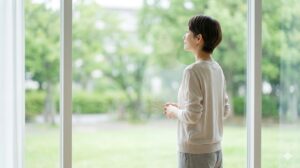 自宅の窓辺で、穏やかな表情で静かに息をつき、自分らしい決断に安らぎを感じる30代後半の日本人女性。希望の光。